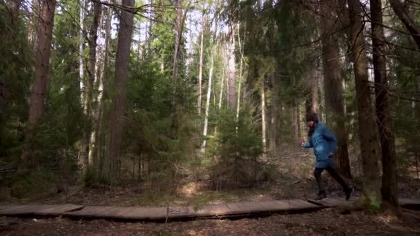 Una mujer con un impermeable azul corre por el camino del bosque. Entrenamiento. Lento. — Vídeos de Stock