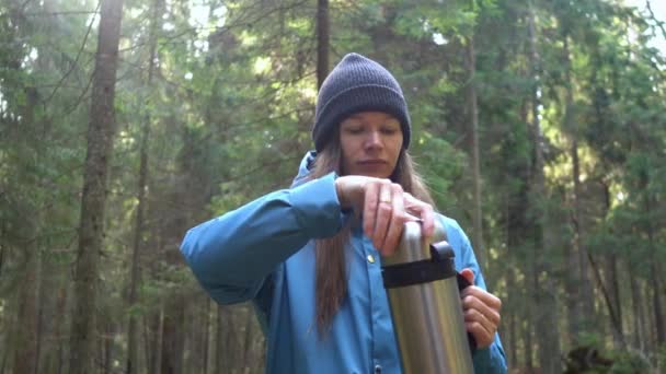 Vrouw drinken warme thee uit thermoskan zittend op de boom in het bos. — Stockvideo