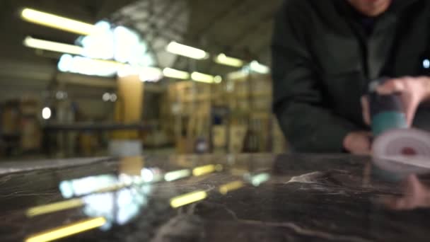 Trabajador irreconocible en una chaqueta verde pule una mesa de mármol en una fábrica. En la mesa de mármol el reflejo de las lámparas. La cámara se mueve en el control deslizante. Super cámara lenta — Vídeos de Stock