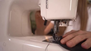 Kadın dikiş makinesine koruyucu maske dikiyor. Kadın evde çalışıyor..