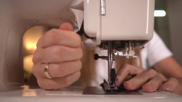 Woman sews a black protective mask on a sewing machine. Cuts black threads with scissors. — Stock Video