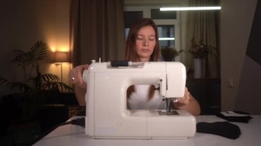 Kadın dikiş makinesini evde dolduruyor.