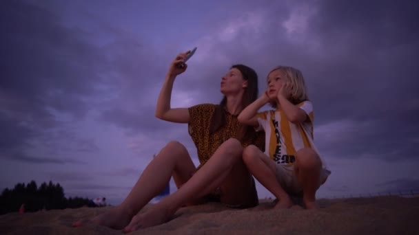 Mamá e hijo se sientan en la playa y toman fotos como un avión aterrizando por encima de ellos — Vídeos de Stock
