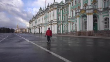 Arka planda Hermitage 'da kaykaylı bir hippi geziyor. Boş sokak. Islak yol.