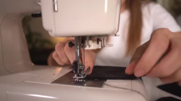 Женщина шьет чёрную защитную маску на швейной машинке дома — стоковое видео