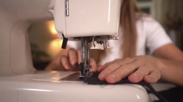 Молодая женщина шьет черную защитную маску на швейной машинке дома — стоковое видео