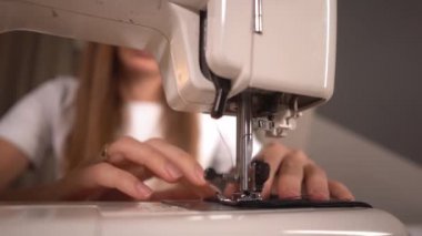 Genç bir kadın dikiş makinesine siyah koruyucu bir maske dikiyor.. 