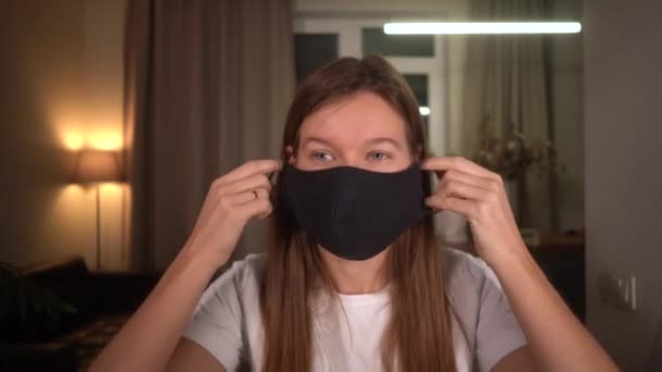 Young woman at home wears a black fabric protective mask that she sewed on a sewing machine — Stock Video