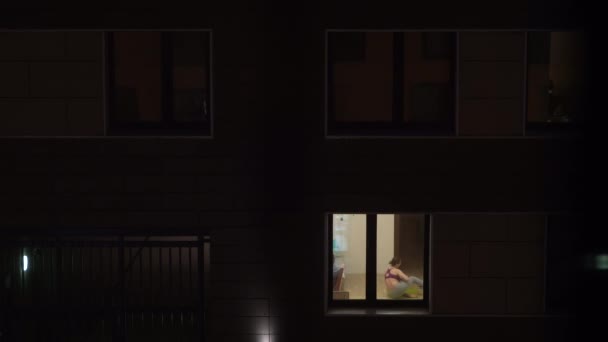 그 여자 애는 아파트에서 요가를 해요. 어느 집의 틀에, 한 창문 안에서 한 소녀가 요가를 하고 있다. — 비디오