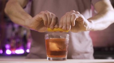 Barmen portakal kabuğunu Negroni kokteyliyle bardağa sıkıştırıyor.