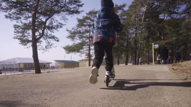 Loira menino montando um chute scooter no parque no ensolarado dia da primavera — Vídeo de Stock
