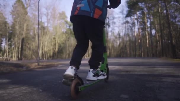 Ragazzo in sella a un calcio scooter nel parco al sole giorno di primavera — Video Stock