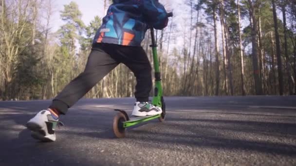 Blonde boy riding an kick scooter in the park at sunny Spring day — Stock Video