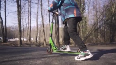 Mutlu çocuk güneşli bahar gününde parkta scooter sürüyor.