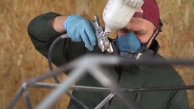 Mavi koruyucu maskeli bir işçi, Metal Ürünleri Havasız Spreyle Boyuyor. Yavaş çekim