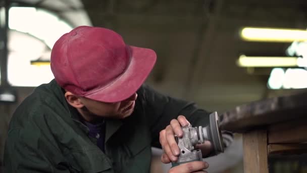 Worker in a green jacket polishes a dark marble table in a factory. In the background is a window and lamps. Super Slow Motion — Stock Video