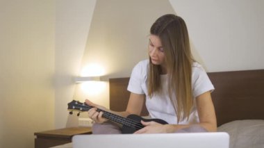 Genç Mutlu Kadın evde dizüstü bilgisayar kullanarak gitar çalmayı öğreniyor. Çevrimiçi Eğitimde Uzaklık Öğrenme