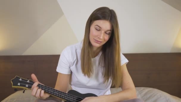 Giovane donna che impara a giocare l'ukulele utilizzando il computer portatile a casa. Istruzione online sull'apprendimento a distanza — Video Stock