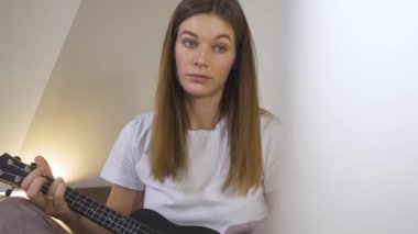 Bilgisayarla ukulele oynayan güzel bir kadın, karantinada online kursla oynamayı öğreniyor. Çevrimiçi Eğitimde Uzaklık Öğrenme