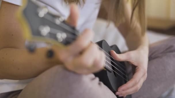Закройте руки, молодая женщина играет на укулеле. Дистанционное обучение онлайн — стоковое видео