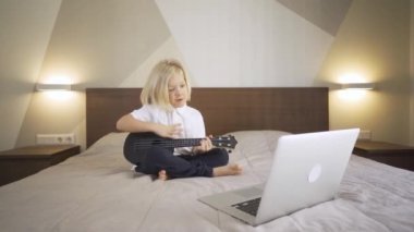 Uzaktan öğrenme çevrimiçi eğitim. Evde gitar çalmayı ve dizüstü bilgisayarda şarkı söylemeyi öğrenen sevimli bir çocuk.. 