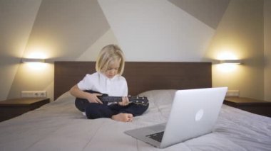 Uzaktan öğrenme çevrimiçi eğitim. Bir anaokulu çocuğu evde dizüstü bilgisayarla gitar çalmayı öğreniyor..