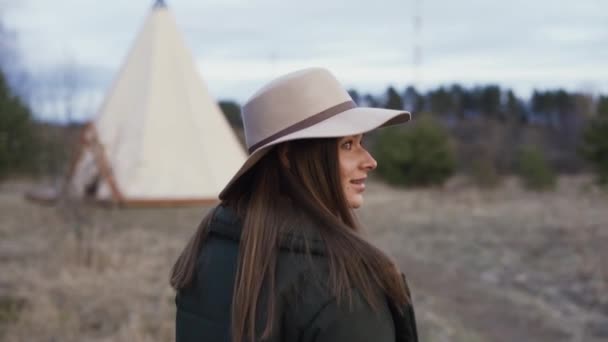 Ung vacker leende kvinna vandrar genom fältet mot Teepee på våren vintern hösten glamping semester — Stockvideo