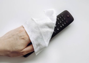 TV uzaktan kumandasını dezenfekte etmek için antibakteriyel ıslak mendil kullanan bir adamın el görüntüsünü kapat.