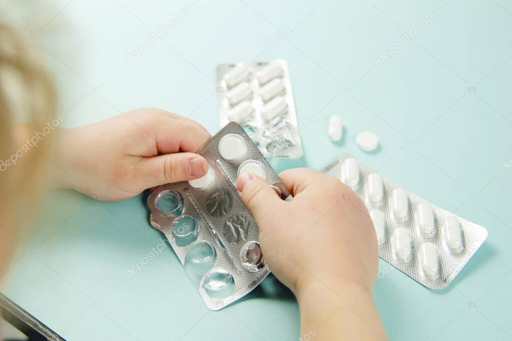 Close up view of child`s hands with blister pack, young child play alone with pills tablets at home.  Keep away from children reach concept. No medicine cabinet, raise awareness.