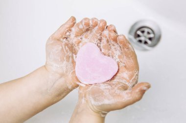 Kişisel hijyen hizmetinin önemi. Kirli elleri pembe kalp şeklinde sabun çubuğuyla yıkayan çocuk manzarası. Bol köpüklü. Boşluğu kopyala.