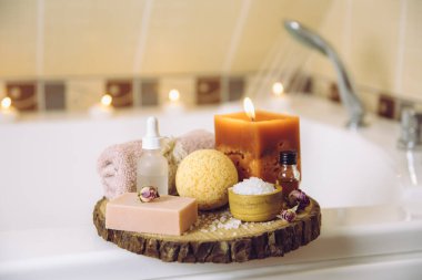 Ev yapımı spa ürünleri ahşap disk tepsisinde: sabun, banyo bombası, aroma banyosu tuzu, zaruri ve masaj yağları, mum yakma, küvet havlusu, su akışı. Rahatlatıcı konsept.