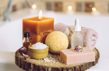 Ev yapımı spa ürünleri ahşap disk tepsisinde: sabun, banyo bombası, aroma banyosu tuzu, zaruri ve masaj yağları, mum yakma, küvet havlusu, su akışı. Rahatlatıcı konsept.
