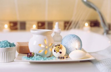 Beyaz seramik tepside spa ürünleri: bir kalıp sabun, banyo bombası, aroma banyosu tuzu, gerekli ve masaj yağları, mum yakma, küvet içinde aroma yağı lambası, su akışı. Kış zamanı kişisel bakım