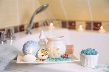 Beyaz seramik tepside spa ürünleri: bir kalıp sabun, banyo bombası, aroma banyosu tuzu, gerekli ve masaj yağları, mum yakma, küvet içinde aroma yağı lambası, su akışı. Kış zamanı kişisel bakım