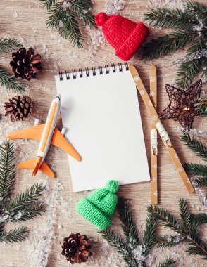 Kış kayak gezisi varış noktasına git. Uçak, kayak, bere, ladin ağacı dalları ve doğal rahat ahşap arka planda boş defter manzarası. Kontrol listesi konsepti.