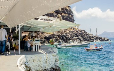 Oia, Santorini / Yunanistan 14JUL2019-Ammoudy Körfezi balıkçı tekneleri ve balık tavernalarıyla. Turistler geleneksel Yunan tavernasında vakit geçirip yemek yiyorlar.