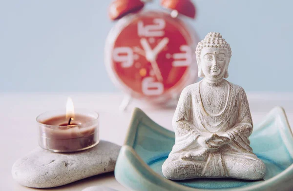 Finding time for self care and balance between body soul and mind. Balance between work and home concept. Lotus pose white color sitting meditation Buddha figurine, red alarm clock on background.