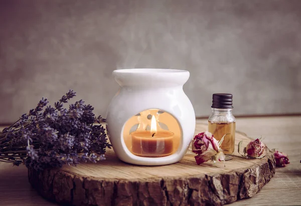 Beyaz seramik aromalı mum aromalı lambanın doğal çam ağacından diskin üzerinde gerekli yağ şişesi ve kuru çiçek yapraklarıyla klasik bir resmi..