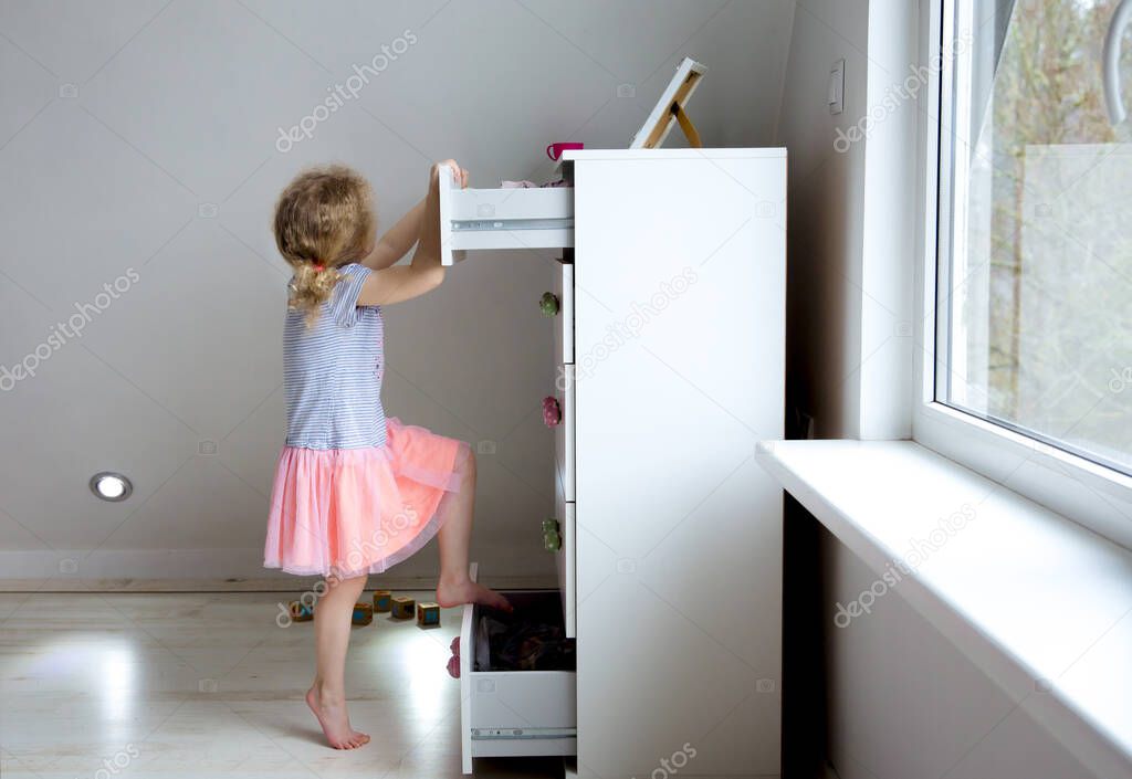 Young girl child climbing on modern high dresser furniture, danger of dresser dipping over concept. Children home hazards. Staged photo.