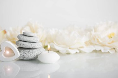 Yığılmış Zen taşları beyaz yanan mum ve bulanık çiçek arkaplanı beyaz parlayan ahşap kalp ışığı. Rahatlatıcı yaşam tarzı kavramı.