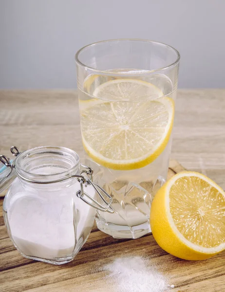 Baking soda in drinking glass with water and lemon juice, health benefits for digestive system concept on natural wooden background.
