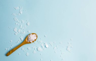 Magnezyum klorür taneleri mavi arka planda kahverengi tahta kaşığın etrafına saçılmış. Ayak banyosu yapmak için magnezyum zengini bir banyo yapmak tüm vücudun yoğun magnezyum çözeltisine maruz kalmasını sağlar..
