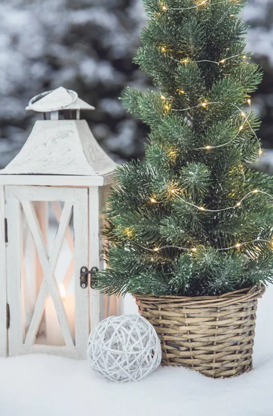 白いワックスキャンドルと白の木製のランタンは 冬には屋外 雪の中で茶色の籐の花の鍋にマイクロLedライトと小さなクリスマスモミの木を点灯します スペースのコピー — ストック写真