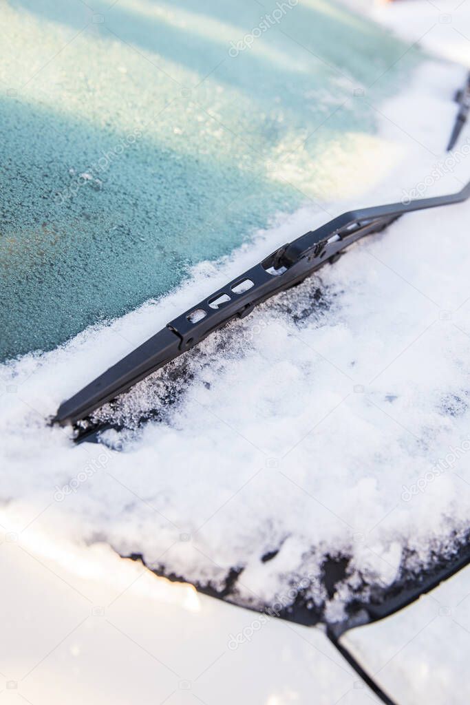 Close up view of a car windscreen wipers or windshield wipers witch are frozen and stuck in snow and ice outdoors in winter.