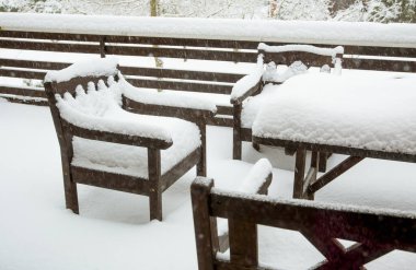 Kahverengi ahşap maun rengi bahçe sandalyeleri ve ev balkonundaki masayı kaplayan temiz kar. Soğuk kış konseptinden sonra bahçe mobilyası bakımı.