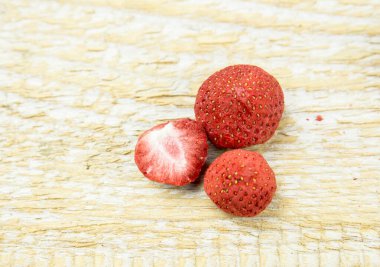 Dondurulmuş bütün ve yeşil çilek yapraklı çilek parçaları, vitamin dolu sağlıklı atıştırmalık ve doğal ahşap arka planda beslenme.