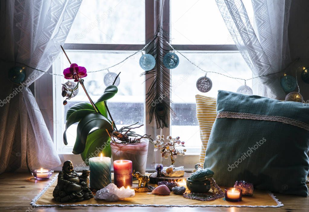 Feng Shui altar at home in living room or bed room. Attracting wealth and prosperity concept. Crystal clusters, wire tree with gemstones, golden Buddah figure on table and window sill. Vibrant colors.