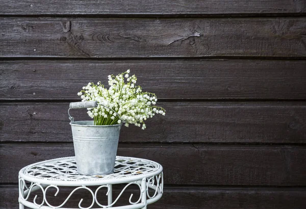 一丛丛白色的切花百合在一个锌桶状的花瓶里 户外的一个白色的花架上 棕色的木制背景 — 图库照片