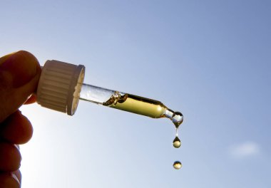 Güneşli bir günde güneşe ve mavi gökyüzüne karşı güzel bir D vitamini ile el ele tutuşan damlacık pipeti. D vitamini kışın güneş yokken sizi sağlıklı tutar..