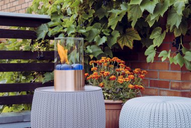 Küçük masa üstü biyo-etanol yakıtlı taşınabilir şömine yangını sonbahar akşamları evdeki balkona ısı ve atmosfer hissi veriyor. Dekoratif üzüm bitkileri kırmızı tuğla duvara tırmanarak büyüyor..